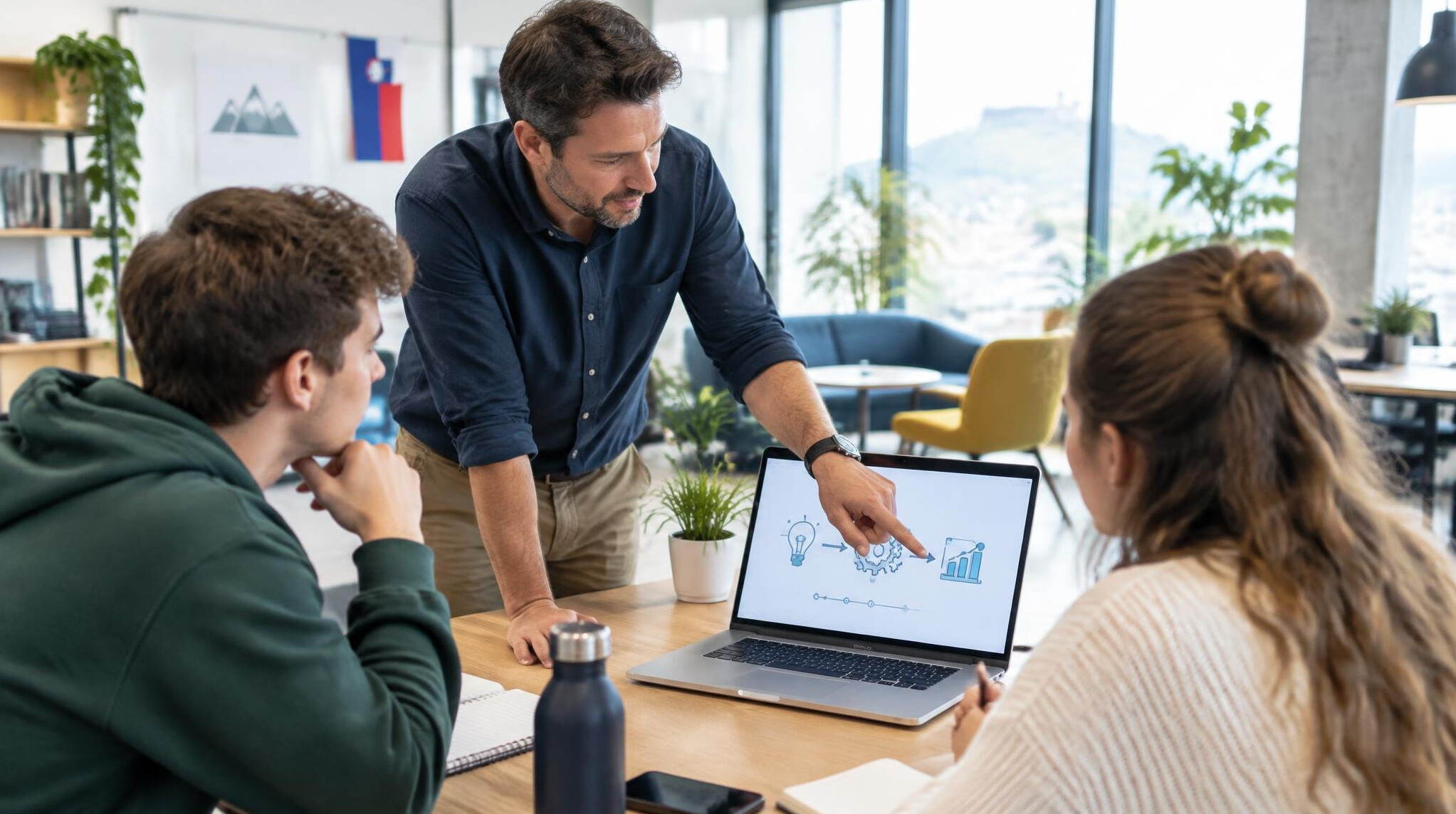 Instructor explaining a concept to students around a table with laptops